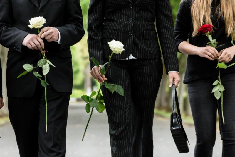 Midsection of family holding roses on road during funeral