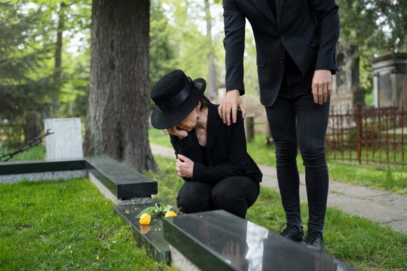 Mourning woman at the cemetery being consoled by mans